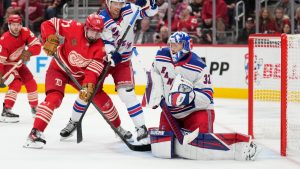 New York Rangers goaltender Jonathan Quick, right, blocks a shot as defenseman Braden Schneider, center, defends Detroit Red Wings center Dylan Larkin during the second period of an NHL hockey game Friday, Nov. 7, 2025, in Detroit. (Ryan Sun/AP)