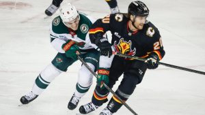 Minnesota Wild's Zeev Buium, left, and Calgary Flames' Blake Coleman chase a loose puck during first period NHL hockey action in Calgary on Thursday, Dec. 4, 2025. (Jeff McIntosh/CP)