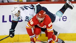 Seattle Kraken's Josh Mahura, top, is checked by Calgary Flames' Joel Farabee during first period NHL hockey action in Calgary on Thursday, Dec. 18, 2025. (Jeff McIntosh/CP)