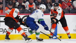 Vancouver Canucks' Conor Garland, centre, plays the puck past Philadelphia Flyers' Nick Seeler (24) and Carl Grundstrom (91) during the first period of an NHL hockey game, Monday, Dec. 22, 2025, in Philadelphia. (Derik Hamilton/AP)