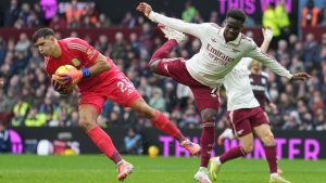 Aston Villa's goalkeeper Emiliano Martinez, left, makes a save ahead of Arsenal's Bukayo Saka during the English Premier League match between Aston Villa and Arsenal in Birmingham, England, Saturday, Dec. 6, 2025. (AP Photo/Dave Shopland)