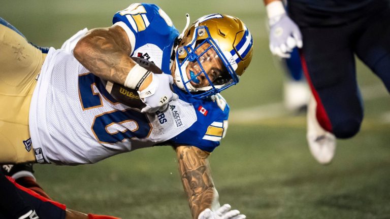 Winnipeg Blue Bombers' Brady Oliveira (20) is tripped up during CFL action against the Montreal Alouettes, in Montreal on Thursday, Aug. 21, 2025. (Christopher Katsarov/CP)