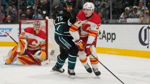 Calgary Flames defenseman Yan Kuznetsov, right, passes the puck against San Jose Sharks right wing Ryan Reaves (75) during the first period of an NHL game in San Jose, Calif., Tuesday, Dec. 16, 2025. (AP Photo/Jeff Chiu)