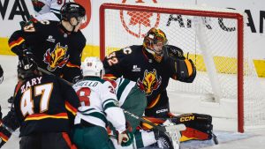 Minnesota Wild's Ryan Hartman, centre hidden, falls as Calgary Flames goalie Dustin Wolf stops a shot during first period NHL hockey action in Calgary on Thursday, Dec. 4, 2025. (Jeff McIntosh/CP)