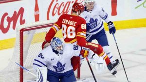 Calgary Flames' Joel Farabee, centre, is pushed into Toronto Maple Leafs goalie Joseph Woll by Troy Stecher, during first period NHL hockey action in Calgary, Monday, Feb. 2, 2026. (Larry MacDougal/CP)