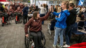 Wheelchair curling athlete Ina Forrest high-fives a passenger as Canadian athletes parade through the boarding gates of Terminal 1 at Toronto Pearson International Airport while preparing to board their flight to the Milan-Cortina Paralympic Games, Thursday, Feb. 26, 2026. THE CANADIAN PRESS/Eduardo Lima