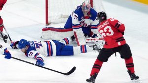 United States goalie Connor Hellebuyck (37) takes a puck off the mask on a shot from Canada's Brad Marchand (63) as United States' Jaccob Slavin (74) defends during the second period of the men's gold medal hockey game at the 2026 Winter Olympics, in Milan, on Sunday, Feb. 22, 2026. (Darryl Dick/CP)
