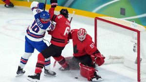 Canada goalie Jordan Binnington (50) makes the save as Canada's Travis Sanheim (6) is checked by United States' JT Miller (10) during the first period of the men's gold medal hockey game at the 2026 Winter Olympics, in Milan. (Darryl Dyck/THE CANADIAN PRESS)