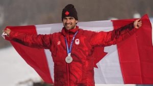 Silver medallist Eliot Grondin celebrates with a Canadian flag after the men's snowboard cross finals at the 2026 Winter Olympics, in Livigno, Italy, Thursday, Feb. 12, 2026. (Lindsey Wasson/AP Photo)