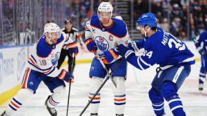 Edmonton Oilers' Zach Hyman (18) moves the puck around Connor McDavid (97) and Toronto Maple Leafs' Auston Matthews (34) during first period NHL hockey action in Toronto on Saturday, Dec. 13, 2025. (Frank Gunn/CP)