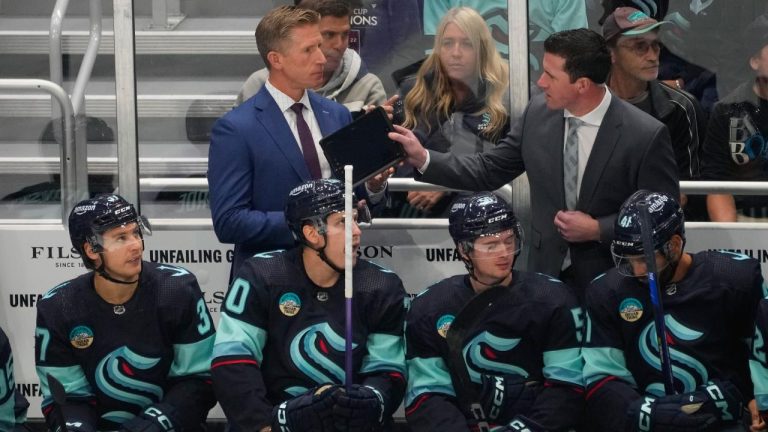 Seattle Kraken head coach Dave Hakstol, back left, is handed a tablet during the first period of an NHL hockey game against the Colorado Avalanche, Tuesday, Oct. 17, 2023, in Seattle. (Lindsey Wasson/AP)