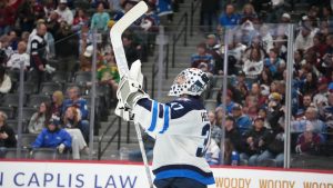 Winnipeg Jets goaltender Connor Hellebuyck raises his stick in celebration as time runs out in the third period of an NHL hockey game against the Colorado Avalanche Saturday, March 28, 2026, in Denver. (David Zalubowski/AP)
