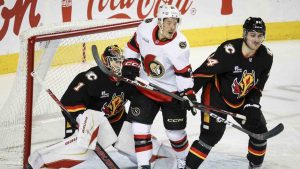 Ottawa Senators' Nick Cousins, centre, is checked by Calgary Flames' Brayden Pachal, right, in front of goalie Devin Cooley during second period NHL action in Calgary on March 5, 2026. (Jeff McIntosh/CP)
