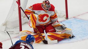 Colorado Avalanche centre Nathan MacKinnon, front, puts a shot on Calgary Flames goaltender Dustin Wolf in the first period of an NHL hockey game Thursday, April 9, 2026, in Denver. (David Zalubowski/AP)
