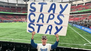 Barry Walker, 75, holds a sign prior to an MLS soccer match between the Vancouver Whitecaps and Sporting Kansas City in Vancouver on Friday, April 17, 2026. Walker has held the same sign for every Whitecaps game this season, encouraging the team to stay in Vancouver as rumours continue to swirl around the future of the Major League Soccer club. (Brieanna Charlebois/CP)