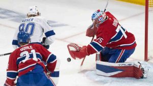 Montreal Canadiens goaltender Jakub Dobes (75) makes a save against Tampa Bay Lightning's J.J. Moser (90) as Canadiens' Kaiden Guhle (21) defends during first period NHL playoff hockey action in Montreal on Friday, May 1, 2026. (Christinne Muschi/CP)