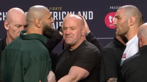 Khamzat-Chimaev,-left,-stares-at-Sean-Strickland-seconds-before-he-kicked-him-in-the-leg-at-the-UFC-328-pre-fight-press-conference-as-UFC-president-Dana-White-looks-on-from-the-middle.