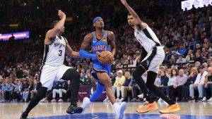 Oklahoma City Thunder guard Shai Gilgeous-Alexander, centre, drives to the basket between San Antonio Spurs forward Keldon Johnson (3) and forward Victor Wembanyama (1) during the second half of an NBA basketball game Tuesday, Jan. 13, 2026, in Oklahoma City. (Nate Billings/AP)