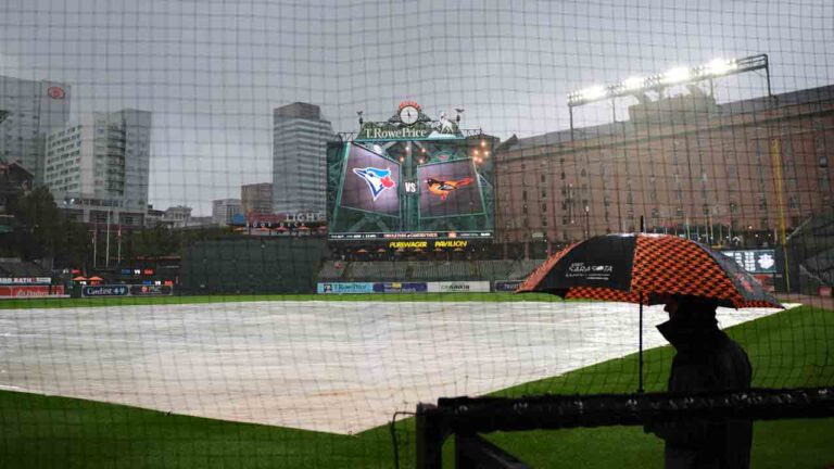 A person stands under an umbrella while it rains as a tarp covers the field ahead of a baseball game between the Baltimore Orioles and the Toronto Blue Jays, Monday, Sept. 21, 2026, in Baltimore. (Stephanie Scarbrough/AP)