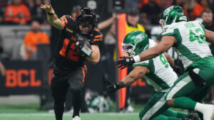 B.C. Lions quarterback Nathan Rourke (12) avoids being sacked by Saskatchewan Roughriders' Mike Rose (42) and James Vaughters (9) and completes a 59 yard pass to Justin McInnis, not seen, during the second half of a CFL football game, in Vancouver, on Friday, Sept. 25, 2026. (Darryl Dyck/CP)