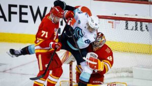 Seattle Kraken's Kaapo Kakko, centre, is checked by Calgary Flames' Simon Nemec, left, into goalie Dustin Wolf during third period NHL hockey action in Calgary on Thursday, Oct. 1, 2026. (Jeff McIntosh/CP)
