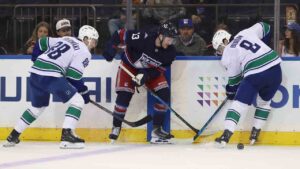 Vancouver Canucks' Jonathan Lekkerimäki, left, and Zeev Buium, right, compete for the puck against New York Rangers' Alexis Lafrenière, center, during the first period of an NHL hockey game Sunday, Oct. 11, 2026, in New York. (Pamela Smith/AP)