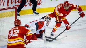 Carolina Hurricanes goalie Brandon Bussi, centre, blocks the net on Calgary Flames' Zayne Parekh, right, as Matvei Gridin tries for the rebound during first period NHL hockey action in Calgary on Sunday, Oct. 18, 2026. (Jeff McIntosh/CP)