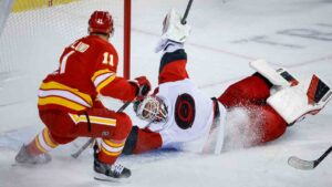 Carolina Hurricanes goalie Brandon Bussi, right, grabs the puck from Calgary Flames' Mikael Backlund during first period NHL hockey action in Calgary on Sunday, Oct. 18, 2026. (Jeff McIntosh/CP)