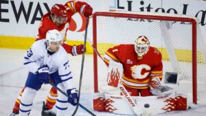 Toronto Maple Leafs' Teddy Blueger (73) tries to deflect the puck past Calgary Flames goalie Devin Cooley (1) as Zayne Parekh (19) checks during first period NHL hockey action in Calgary on Monday, Oct. 26, 2026. (Jeff McIntosh/CP)