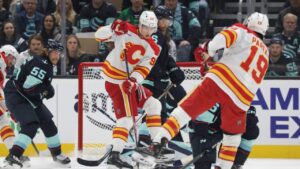 Calgary Flames right wing Matvei Gridin (92) sets a screen as defenceman Zayne Parekh (19) moves the puck and Seattle Kraken defenceman Ryan Lindgren (55) defends during the first period of an NHL hockey game Sunday, Oct. 4, 2026, in Seattle. (AP Photo/Jason Redmond)