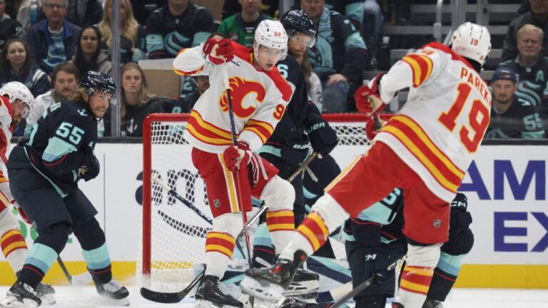 Calgary Flames right wing Matvei Gridin (92) sets a screen as defenceman Zayne Parekh (19) moves the puck and Seattle Kraken defenceman Ryan Lindgren (55) defends during the first period of an NHL hockey game Sunday, Oct. 4, 2026, in Seattle. (AP Photo/Jason Redmond)
