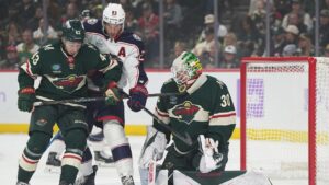 Minnesota Wild goaltender Jesper Wallstedt (30) and defenseman Quinn Hughes (43) defend against a shot as Columbus Blue Jackets center Sean Monahan (23) pressures them during the first period of an NHL hockey game, Sunday, Oct. 18, 2026, in St. Paul, Minn. (AP Photo/Abbie Parr)